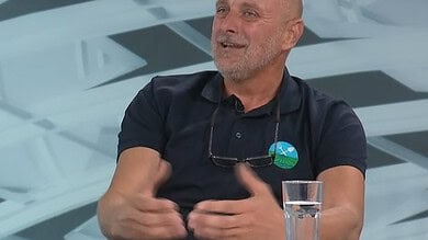 Човек говори на ТВ емисији уз стаклени чаши и намештај у позадини.