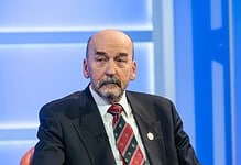 Političar u tamnom odelu sa crvenim prugastim kravatom sedi na panel diskusiji.
