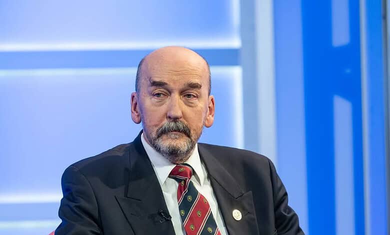 Апел српског православног народа за молитву и духовно укрепљење Србије Političar u tamnom odelu sa crvenim prugastim kravatom sedi na panel diskusiji.