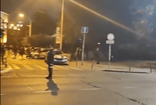 Слика града ноћна сцена са пешацем на раскршћу и возила у позадини.