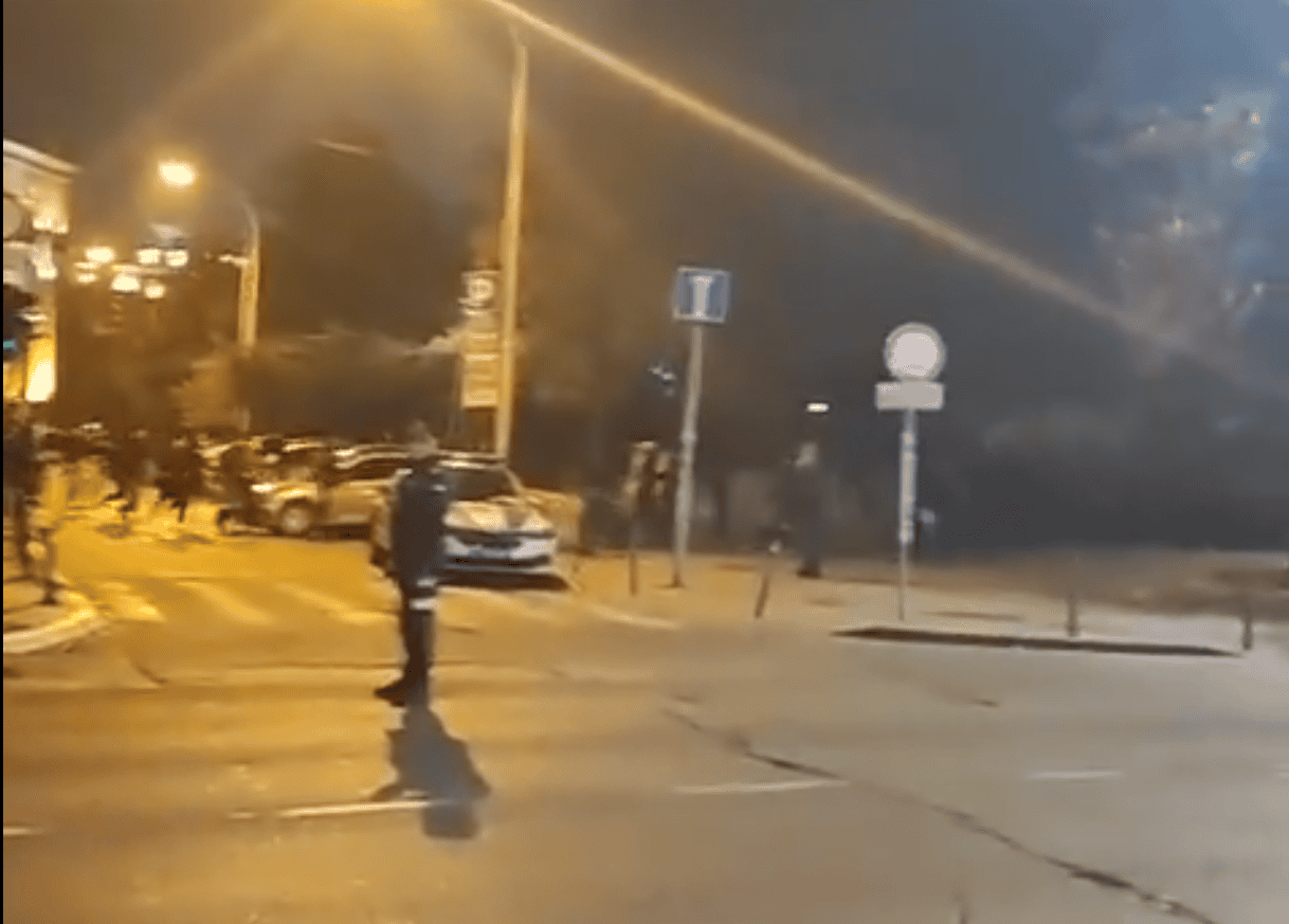 Слика града ноћна сцена са пешацем на раскршћу и возила у позадини.