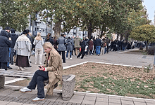 Линија људи чека испред изборне фирме; женa седа на клупи у предворју.