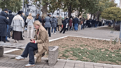 Линија људи чека испред изборне фирме; женa седа на клупи у предворју.