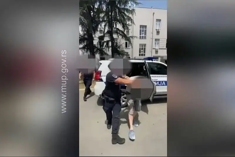 Pohapšeni muškarac i policajci ispred policijske patrulje.