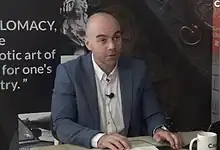 Мушкарц у оделу говори у медијском интервјуу.