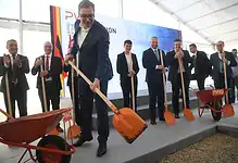 Људи у свечаној атмосфери копају и постављају нову фасаду зграде.