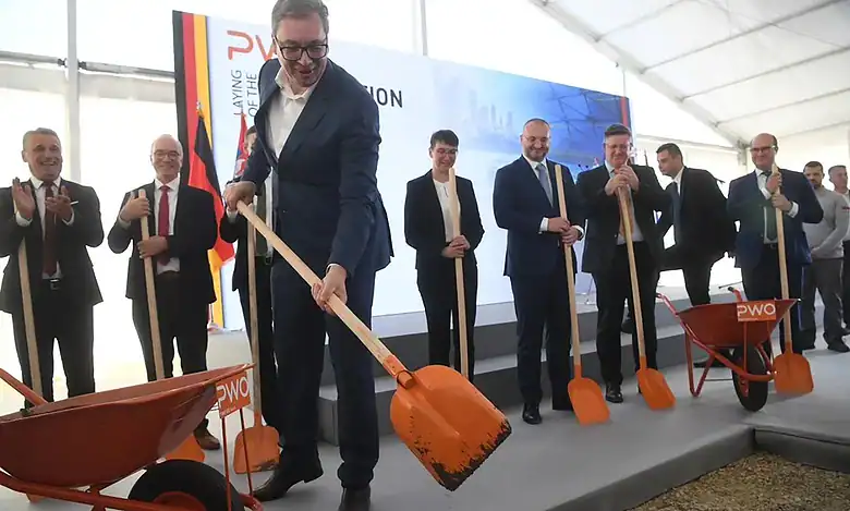 Људи у свечаној атмосфери копају и постављају нову фасаду зграде.