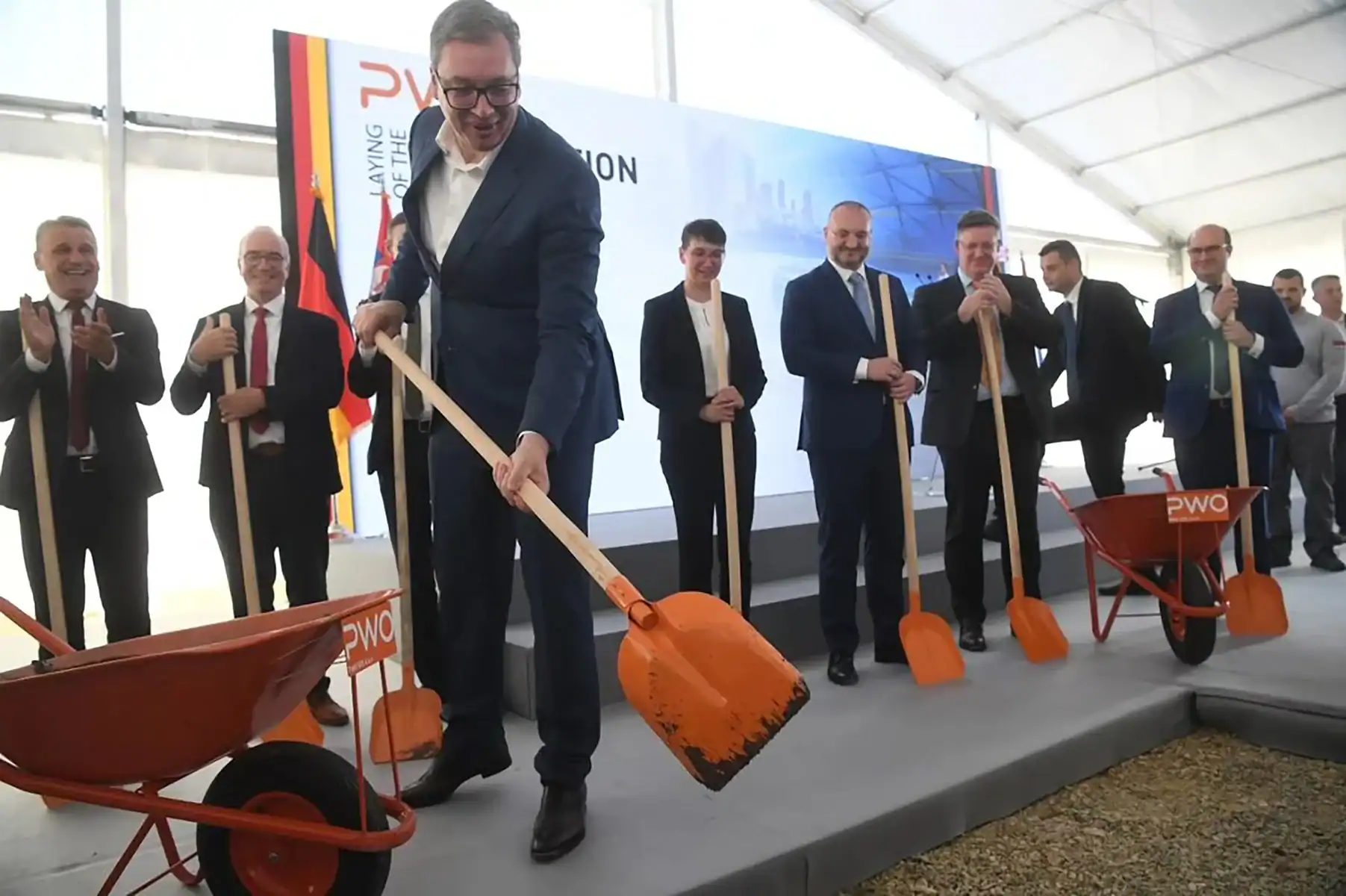 Људи у свечаној атмосфери копају и постављају нову фасаду зграде.