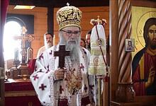 Високи црквени службеник у цркви са крстом и иконама у позадини.