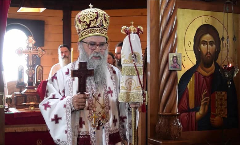 Високи црквени службеник у цркви са крстом и иконама у позадини.
