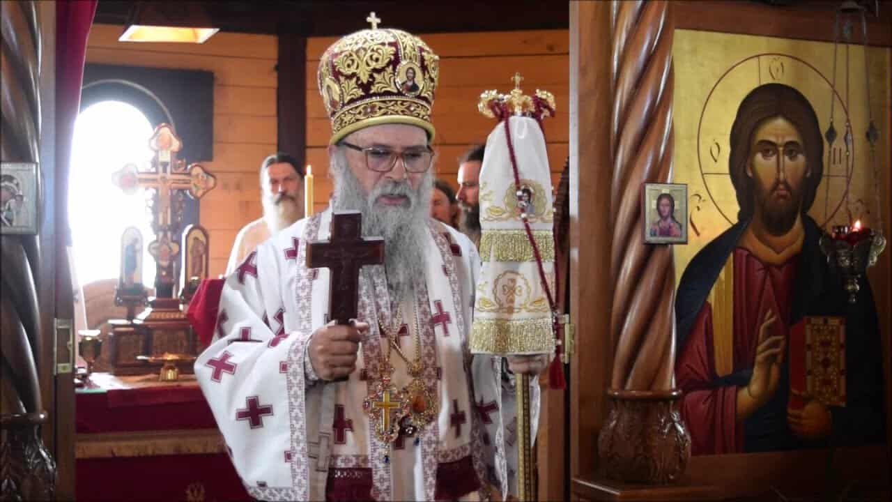 Високи црквени службеник у цркви са крстом и иконама у позадини.
